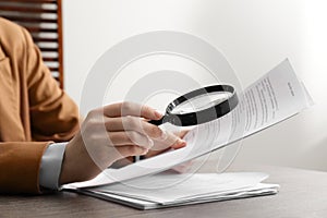 Woman looking at document through magnifier at table indoors, closeup. Searching concept