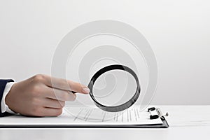 Woman looking at document through magnifier at white table, closeup. Searching concept