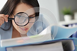 Woman looking at documents in folder through magnifying glass