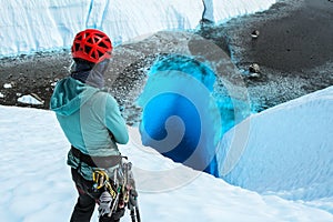 Woman looking down deep blue hole on glacier in Alaska