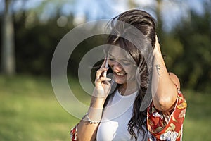 Woman looking down and smiling while talking on the phone outdoors in the nature