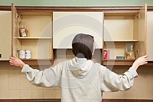 Woman Looking In Empty Food Cupboards