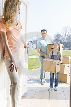Woman looking at family with cardboard boxes entering new home