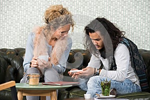 Woman Looking At Friend Using Mobile Phone In Cafe