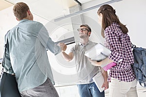 Woman looking at friends greeting while holding hands in university corridor