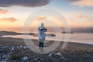 A woman looking at frozen Baikal lake at sunset, Siberia, Russia