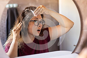 Woman Looking for Gray Hair in the Mirror. Young woman scared of premature aging signs