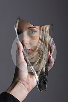 Woman looking at her face in shard of broken mirror