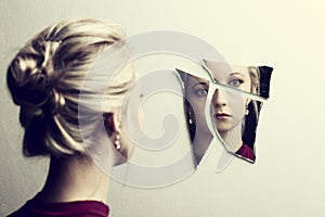 Woman looking at her face in three shards of broken mirror