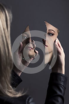 Woman looking at her face in two shards of broken mirror