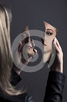 Woman looking at her face in two shards of broken mirror photo