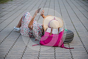 Woman is looking at her smartphone in the middle of the street with her luggage.