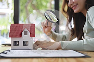Woman looking at the house model with a magnifying glass. Real estate appraisal, land valuation and house selection concept