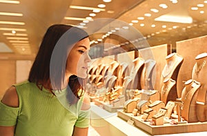 Woman looking at jewelry in store window. Girl chooses silver, gold, diamonds, precious stones