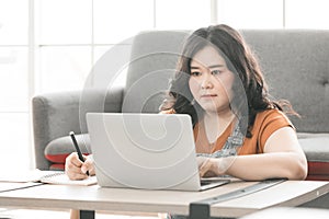 Woman looking at laptop computer and writing on notebook for work or study
