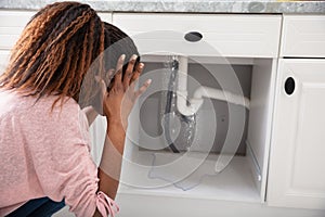 Woman Looking At Leaking Sink Pipe In Kitchen