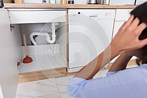 Woman Looking At Leaking Sink Pipe