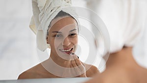 Woman looking in mirror applying long-lasting lipstick on lips