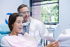 Woman looking at mirror by dentist at medical clinic