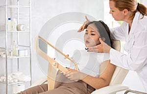 Woman looking at mirror while professional cosmetician explaining her future hardware facial procedure in medical