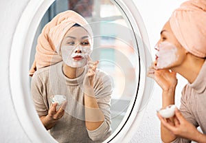 Woman looking at mirror and smoothing cream over face