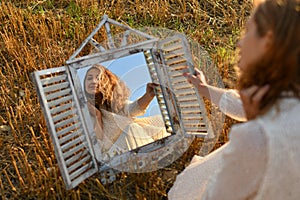 Woman looking into a mirror in a wheat field