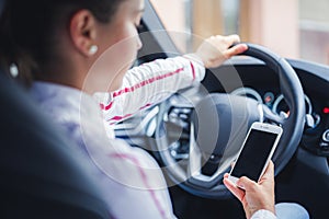 Woman looking at mobile phone while driving a car. Driver using smart phone in car.