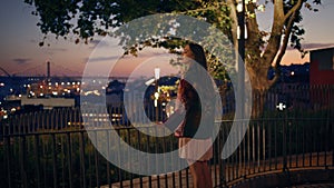 Woman looking night cityscape standing at railings. Girl enjoying twilight sky