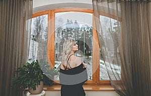 Woman looking through the old window sitting on the window sill. Dressed in stockings