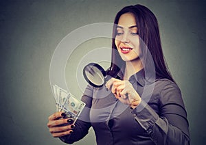 Woman looking at one hundred dollar bills through magnifying glass