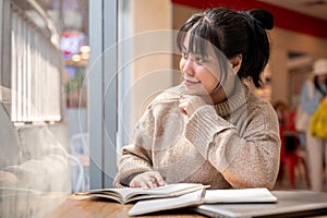 A woman is looking out the window and daydreaming while reading a book in a coffee shop
