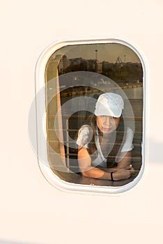 Woman looking out window of ferry boat with white hat