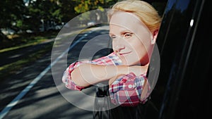 A woman is looking out the window of a traveling car. Enjoy the beautiful scenery, near the forest and the lake. Slow