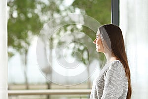 Woman looking outside through window at home photo