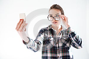 Woman looking over glasses and taking selfie with cell phone