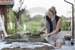 Woman looking at a pallet with stack of sod turf grass rolls, ready for laying in new lawn. Natural grass installation