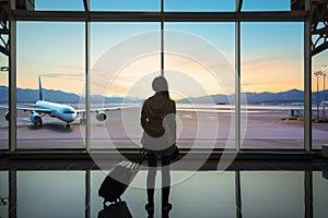 woman looking at plane , standing near the airport window, holding luggage. AI Generated