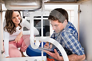 Woman Looking At Plumber View From Under The Sink