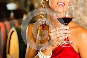 Woman looking at red wine glass in cellar