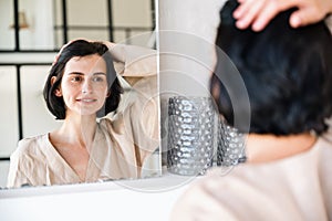 Woman looking at reflection in mirror and fixing hair