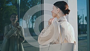 Woman looking reflection window taking off wireless headphones outdoors.