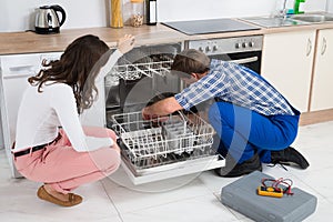 Woman Looking At Repairman Repairing Dishwasher