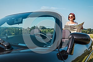 Woman looking a right road in the roadmap during her auto travel in the convertable cabriolet car. Traveling and navigation photo