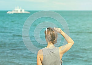Woman looking at the sea. Toned photo of girl watching cruise boat.