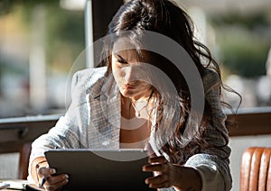 Woman looking with serious expression at digital tablet screen while working in cafe