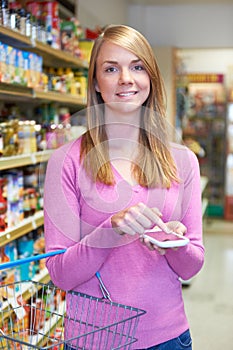 Woman Looking At Shopping List On Mobile Phone In Supermarket