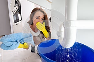 Woman Looking At Sink Pipe Leakage In Kitchen