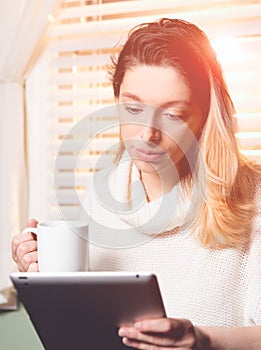 Woman looking at tablet with mug in hand