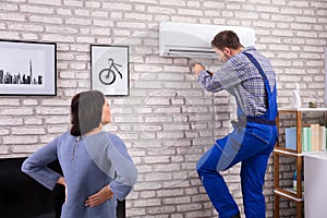 Woman Looking At Technician Repairing Air Conditioner