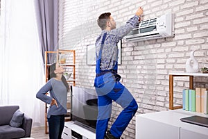 Woman Looking At Technician Repairing Air Conditioner